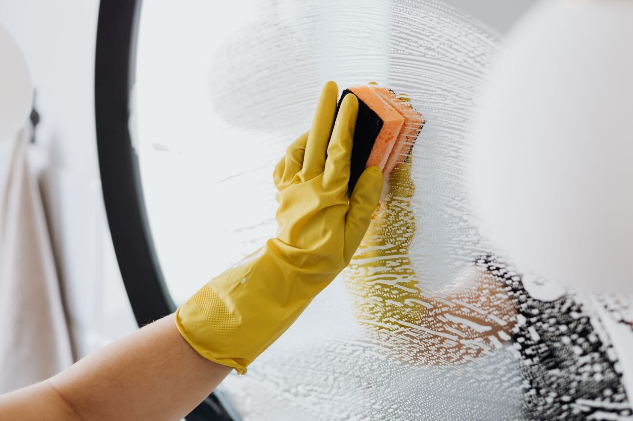About Anonymous person in yellow rubber gloves using simple sponge for cleaning mirror in bathroom