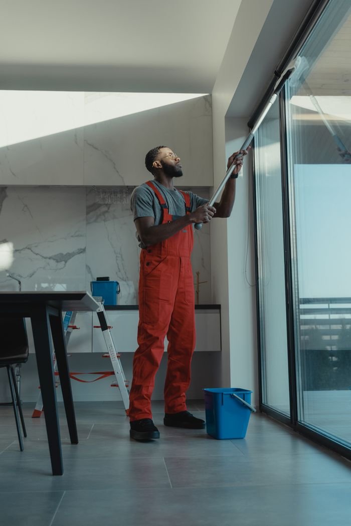 Services A man in coveralls cleans a large window in a stylish, modern home interior.